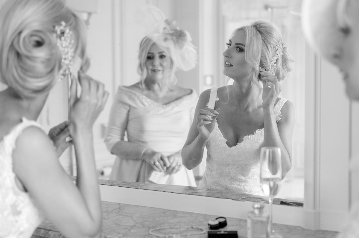 Bride putting on earrings in a large mirror above a marble ledge