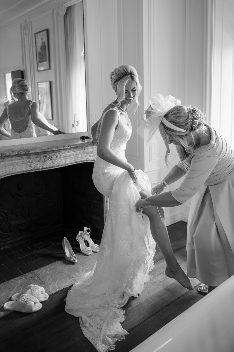 Lady in wedding outfit putting garter on bride's leg