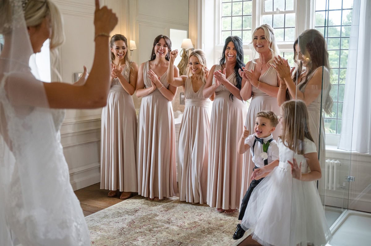 Bridesmaids clapping and smiling as they see the bride in her dress, page boy giving a thumbs up