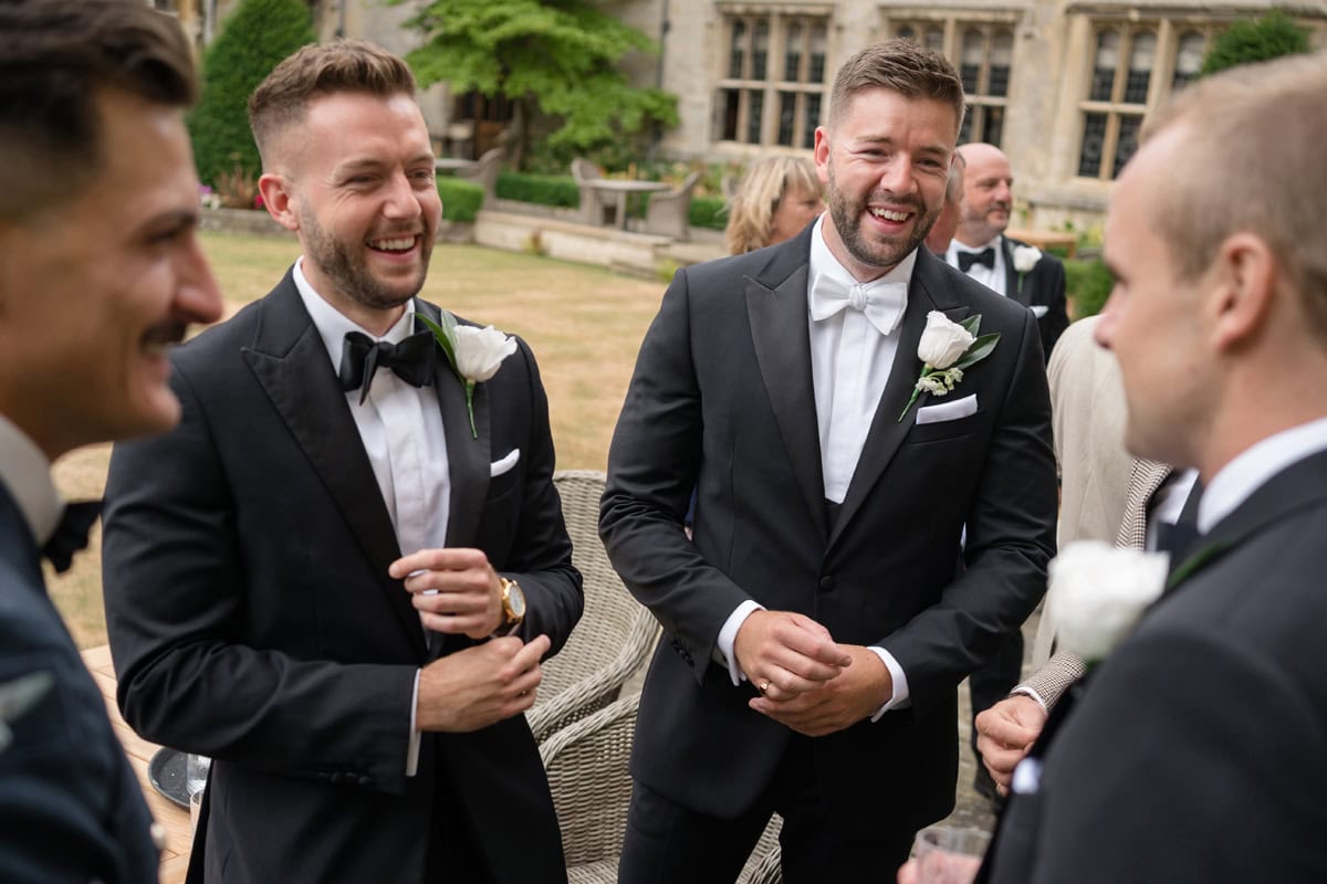 Groom in white tie and best man in black tie chatting with wedding guests
