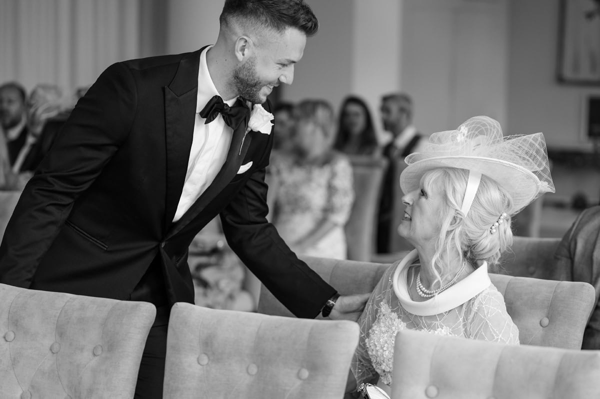 Best man reaching out to greet mother of bride as she takes her seat for wedding ceremony