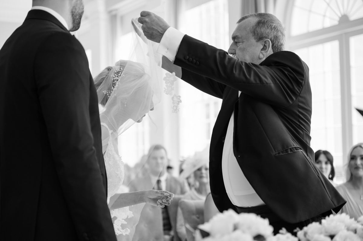 Father of bride lifts bride's veil back as they reach top of aisle