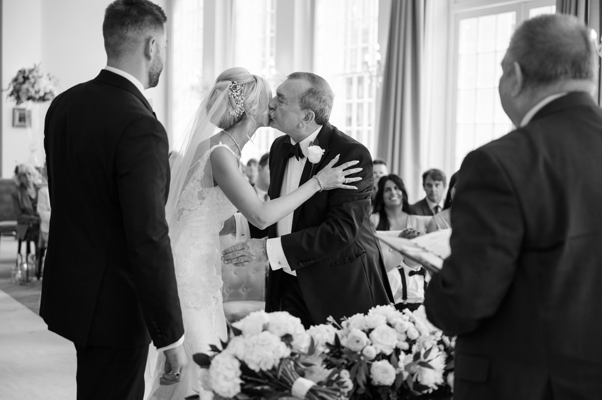 Father of bride kissing his daughter on cheek as he gives her away during wedding ceremony