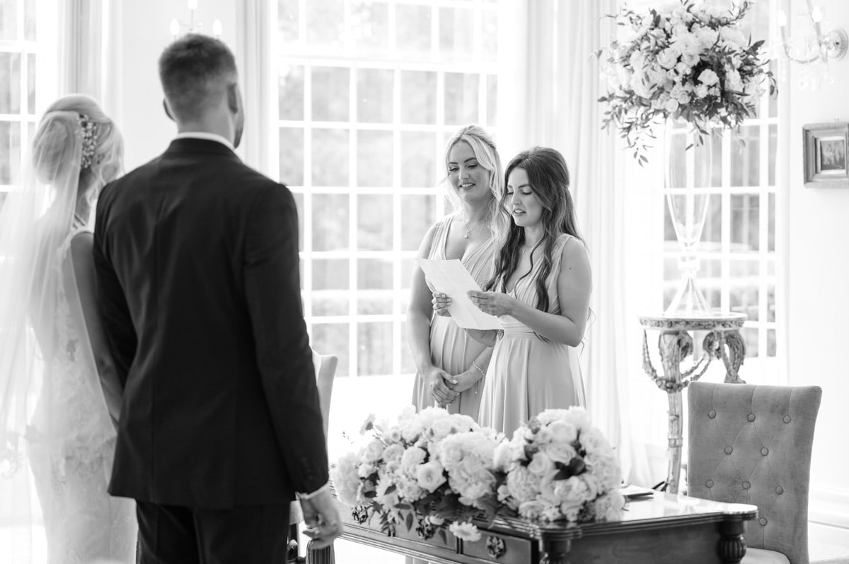 Two bridesmaids doing a wedding ceremony reading as bride and groom look on