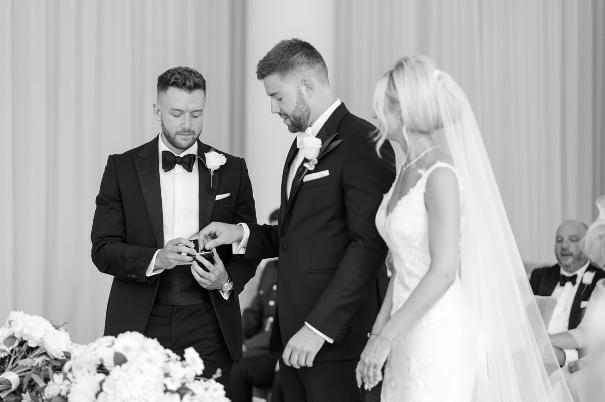 Groom taking ring from the best man while bride watches