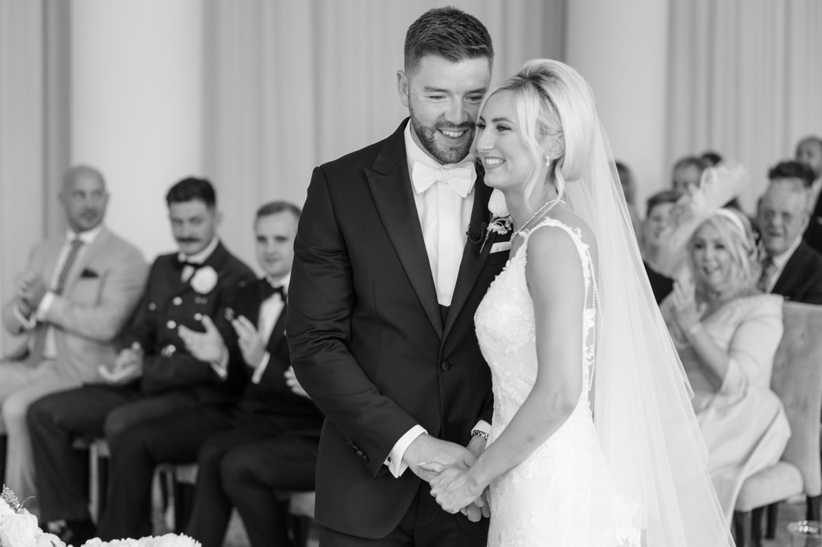 Bride and groom holding hands and looking very happy as they're pronounced husband and wife