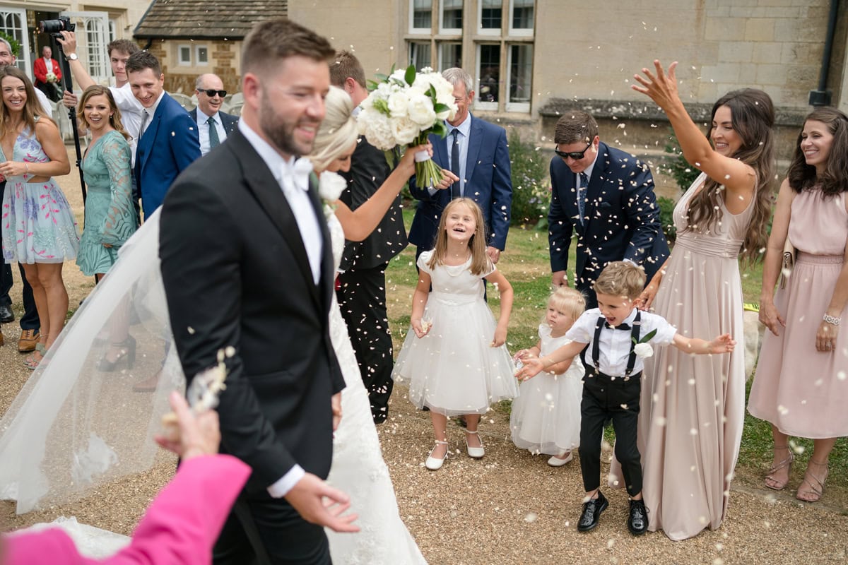 Bridesmaids, flower girls, and pageboy throwing confetti over bride and groom