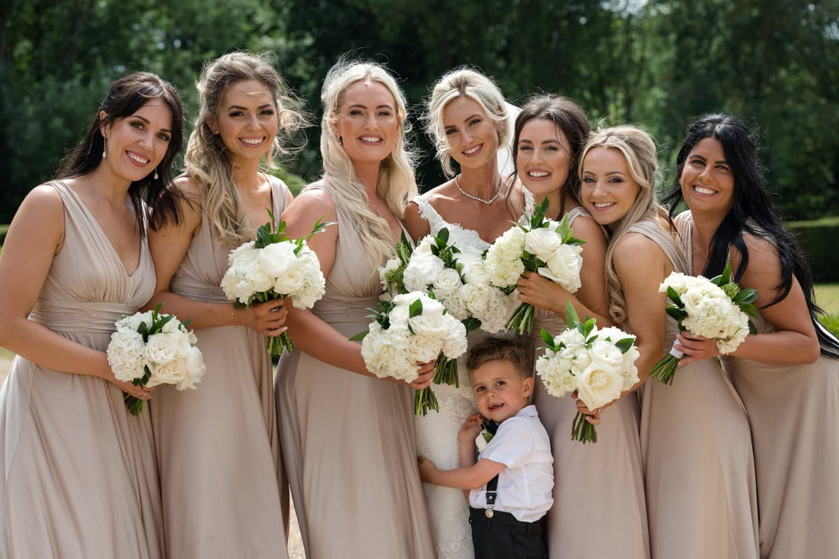 Group photo of bride, bridesmaids wearing neutral colour dresses, and a page boy