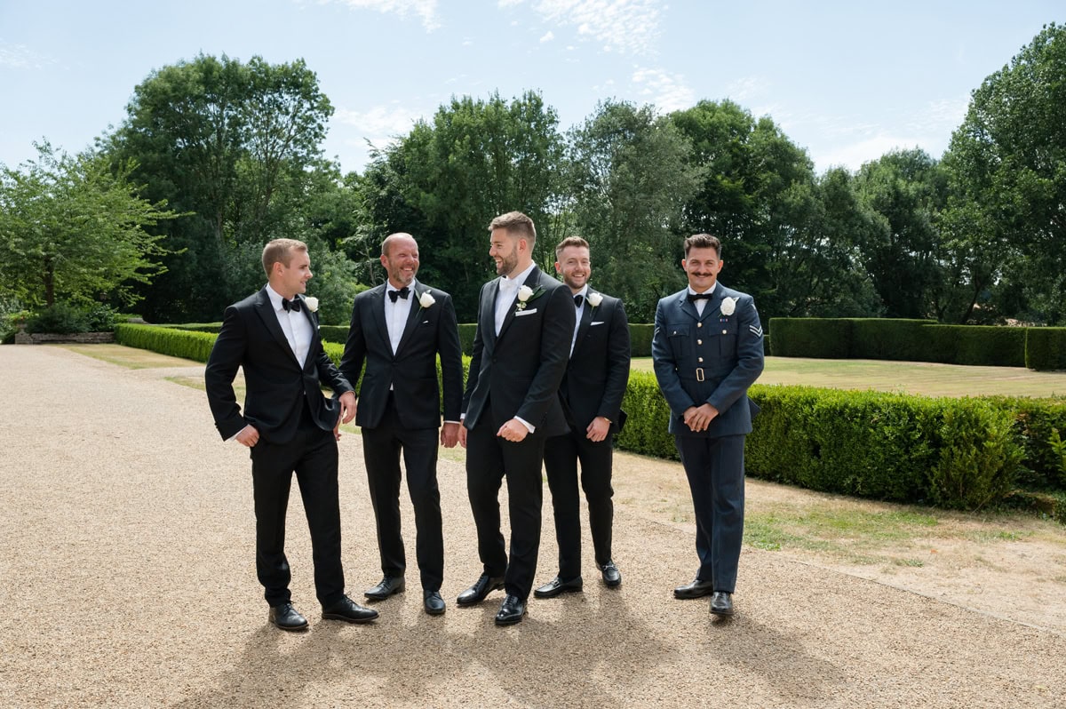 Groomsmen in black tie and one man in military uniform walking and laughing together