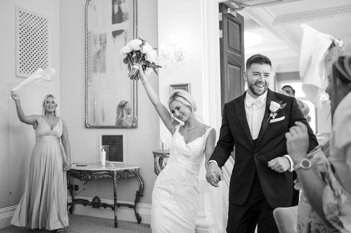 Bride and groom entering a room with guests waving napkins