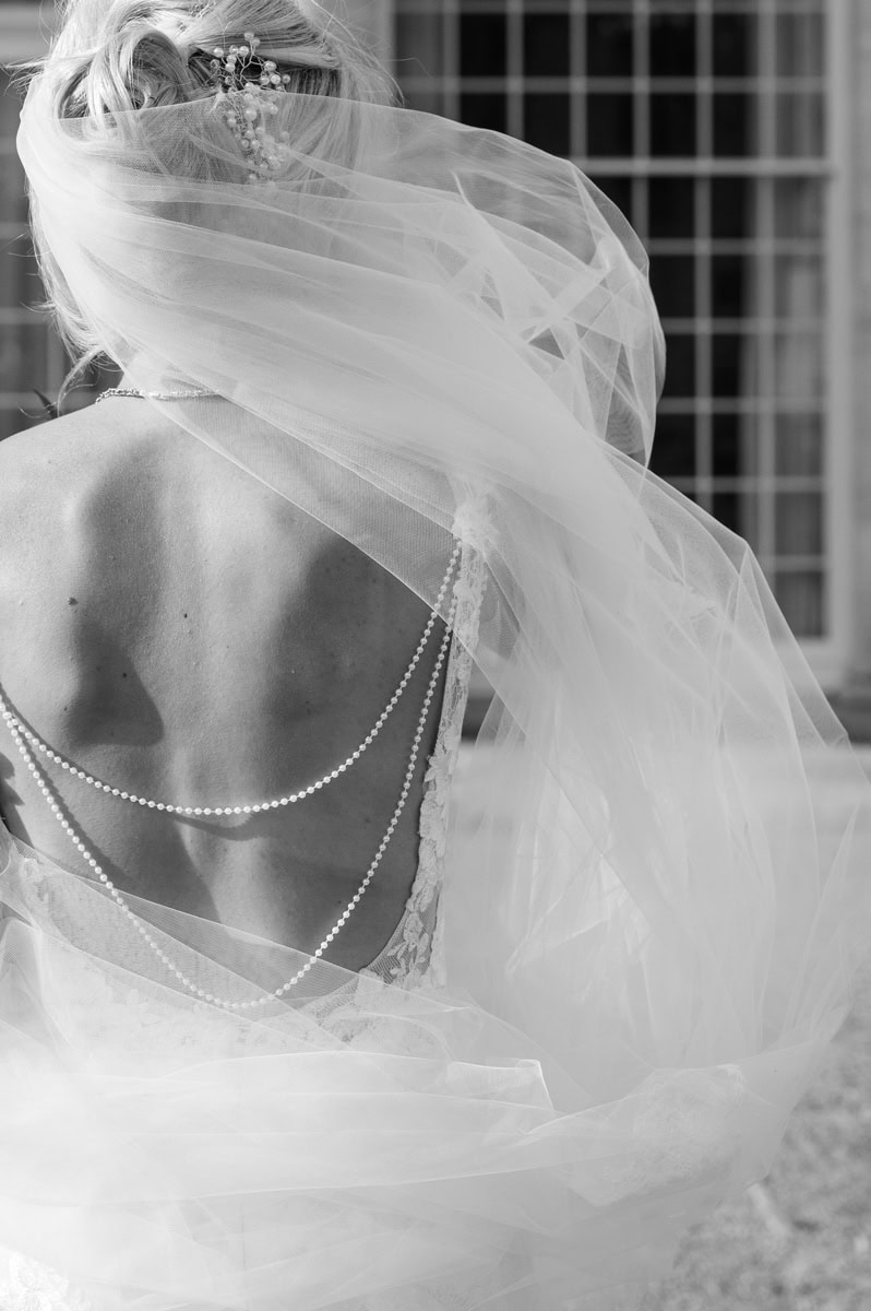 Abstract detail of draped beads on the back of a bride's dress and veil blowing in the wind