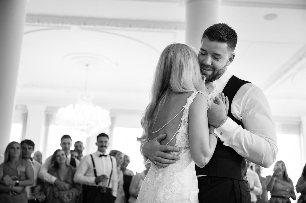 Groom holding the bride for their first dance as wedidng guests look on in the background